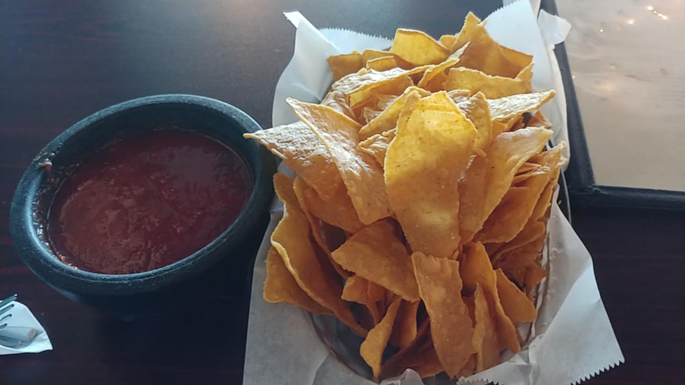 A basket of tortilla chips beside a stone molcajete of red salsa on a dark table