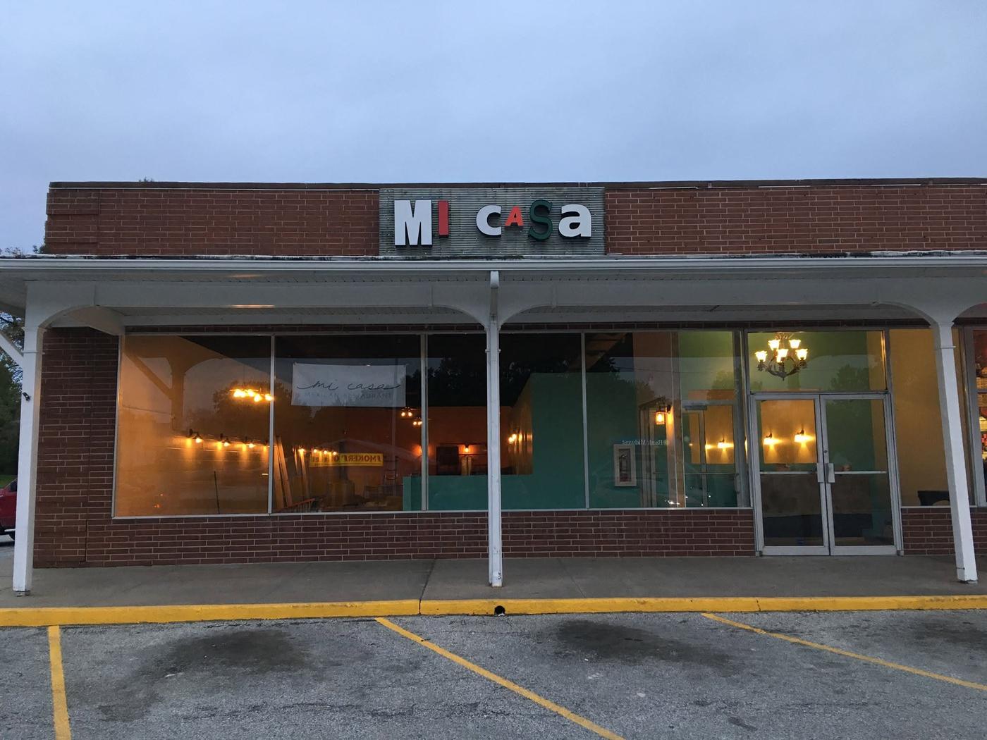 Mi Casa's storefront at dusk, the lit sign over the door and warm light coming through the windows