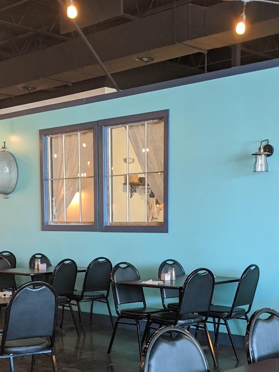 The turquoise dining room wall with two mounted sash windows, a caged sconce and cafe string lights overhead